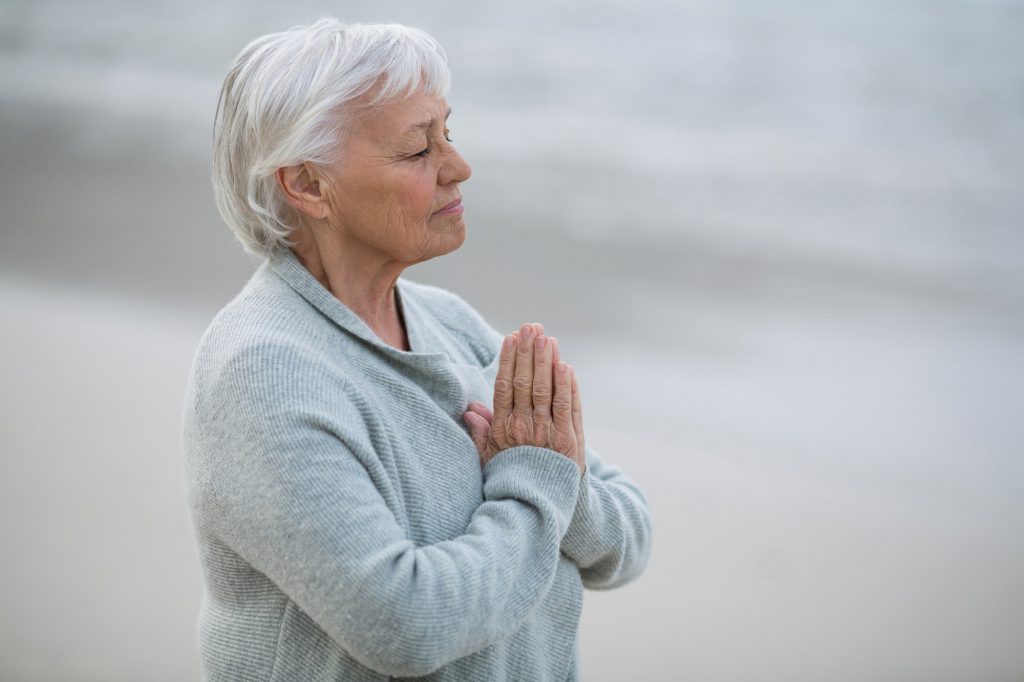 Senior woman praying on the beach